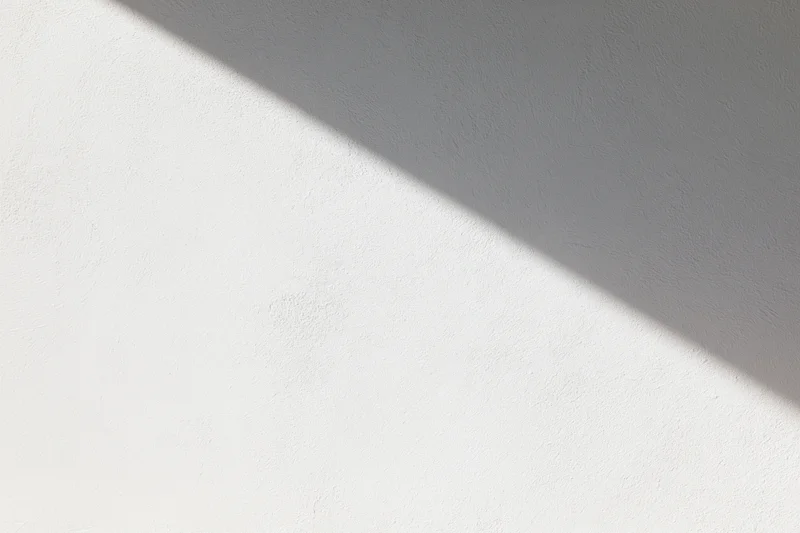 Diagonal sunlight casting shadow across white textured wall interior