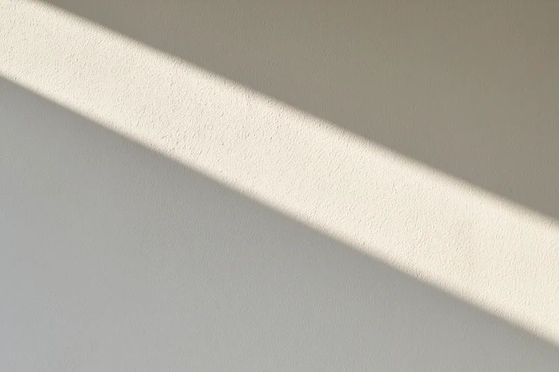 Diagonal band of sunlight across a plain white textured wall indoors