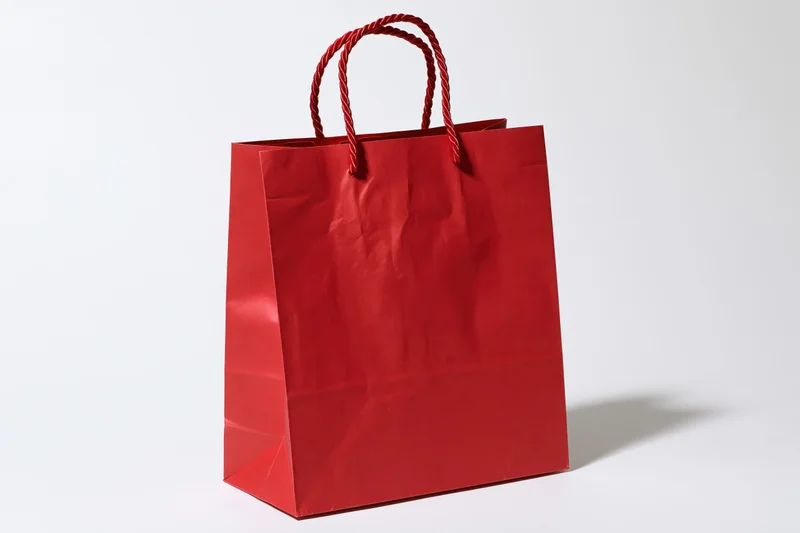 Red glossy paper shopping bag with twisted rope handles on white background