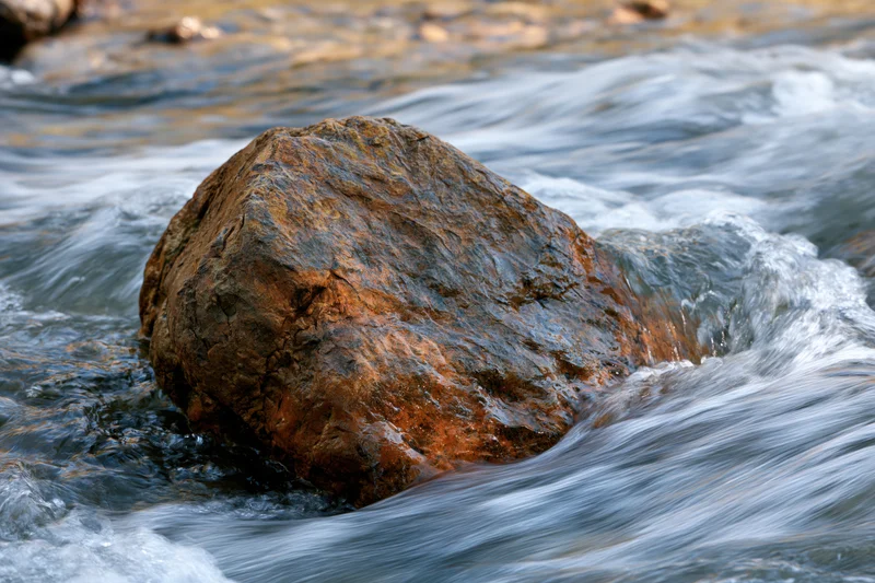 Large wet amber-brown rock in flowing river water