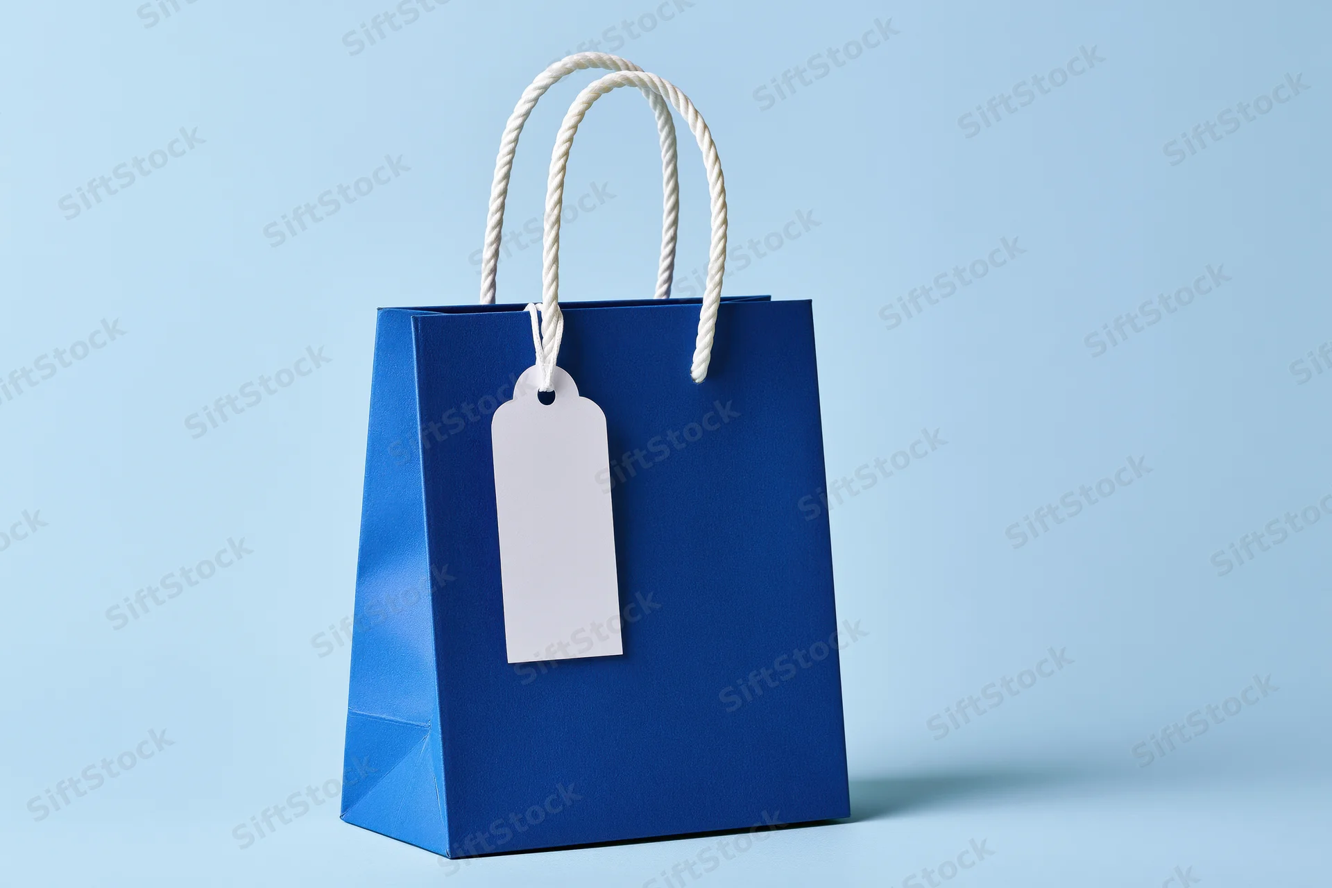 Cobalt blue paper shopping bag with white rope handle and blank tag on light blue background