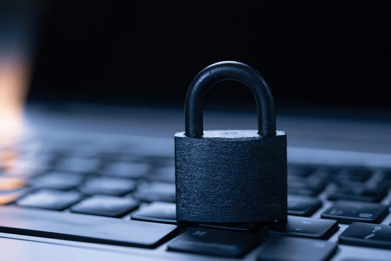 Black metal padlock resting on laptop keyboard in dim blue light