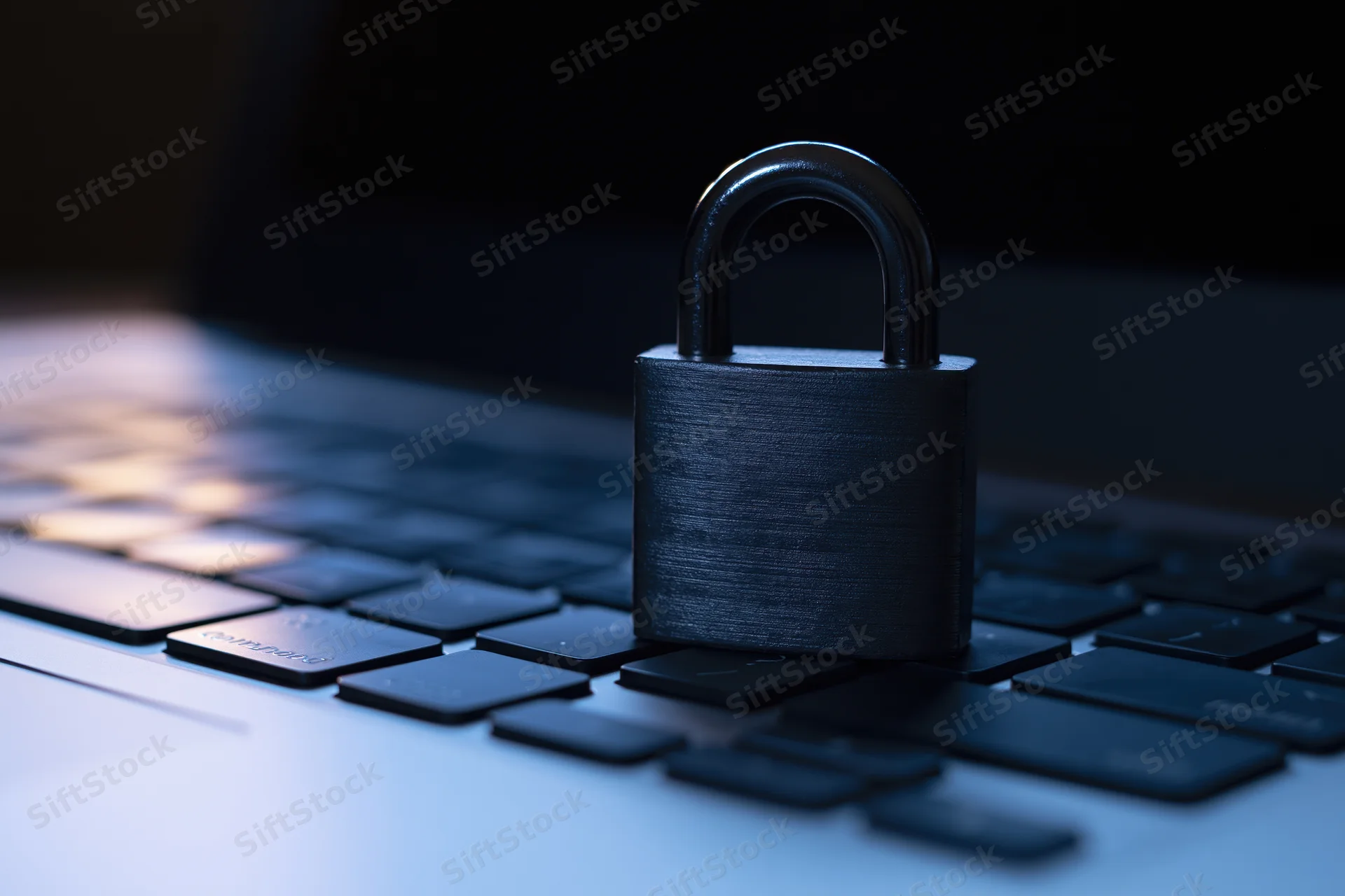 Black metal padlock resting on laptop keyboard in dim blue light