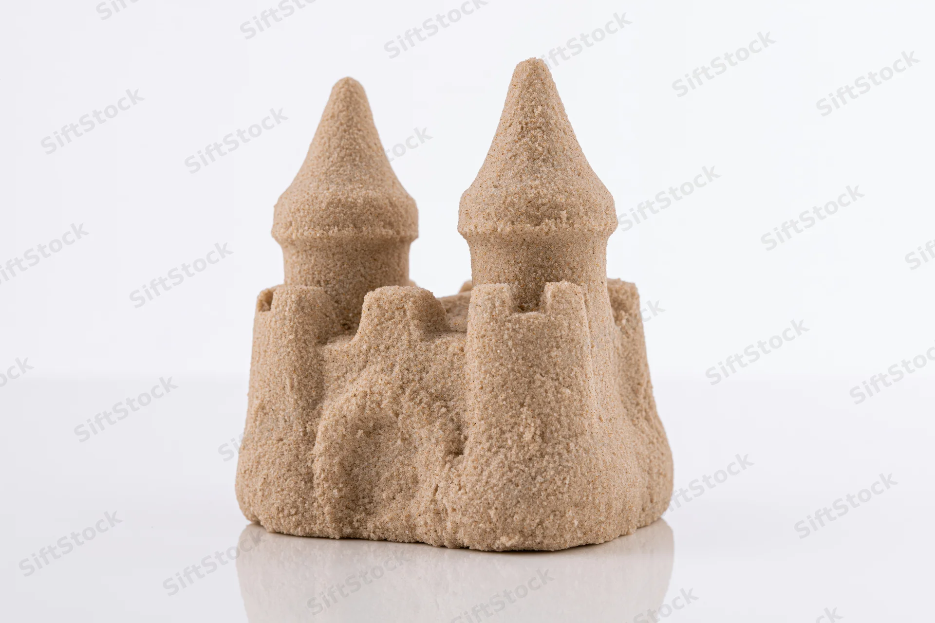 Small molded sand castle with two conical towers and crenelations on white surface
