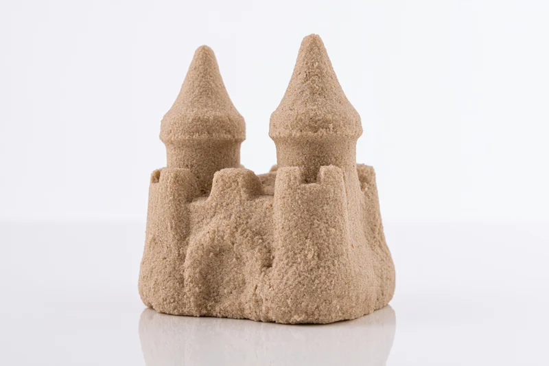 Small molded sand castle with two conical towers and crenelations on white surface