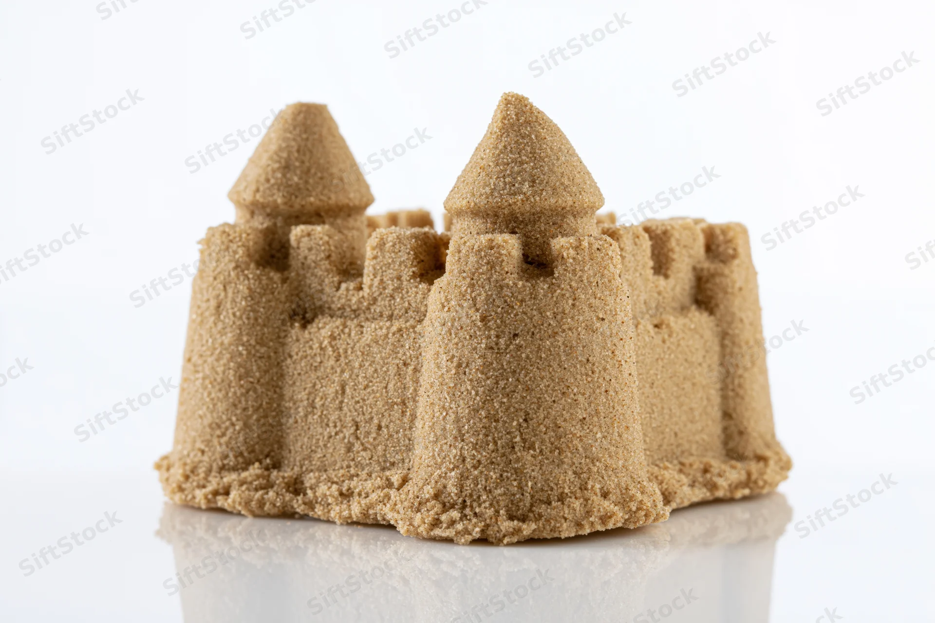 Molded sugar sandcastle with two conical towers and crenel on reflective white surface
