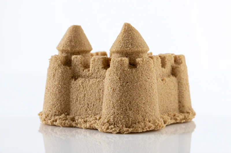 Molded sugar sandcastle with two conical towers and crenel on reflective white surface