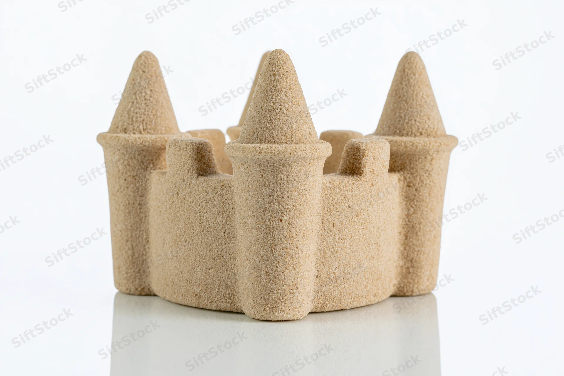 Molded sand castle with conical towers and crenelations on white surface