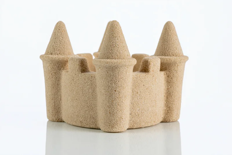 Molded sand castle with conical towers and crenelations on white surface