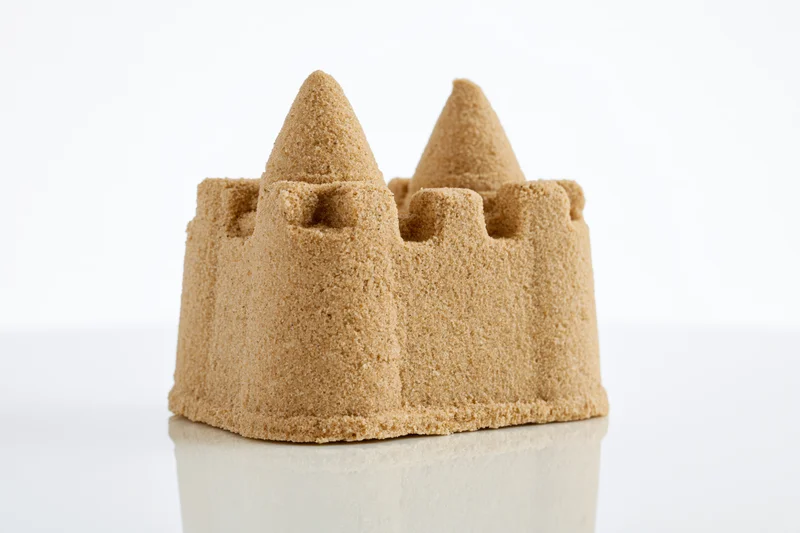 Small molded sandcastle with two conical towers and crenelations on a reflective white surface