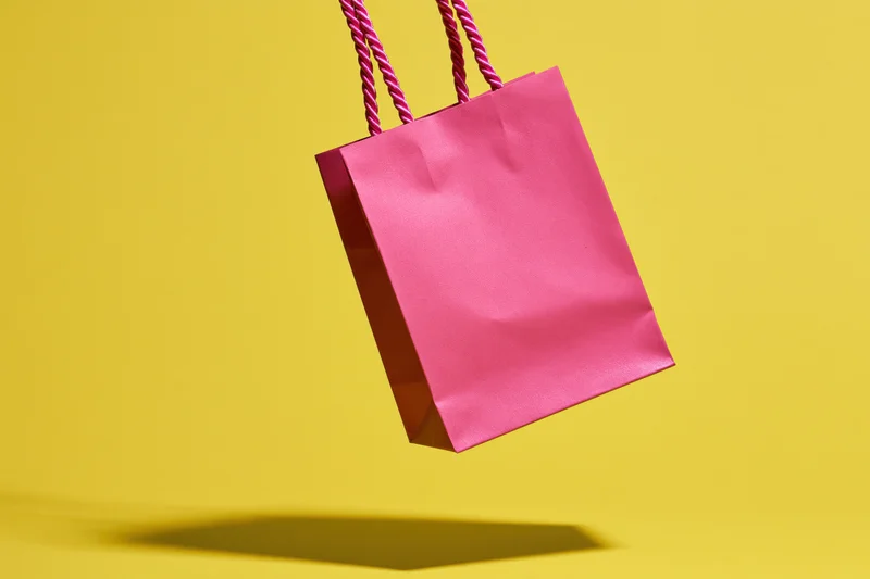 Pink paper shopping bag floating against yellow background with shadow below