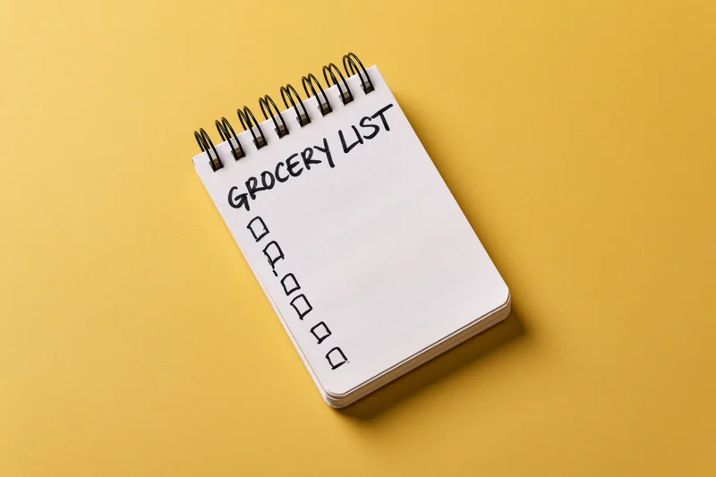 Spiral-bound notepad with grocery list and checkboxes on yellow surface