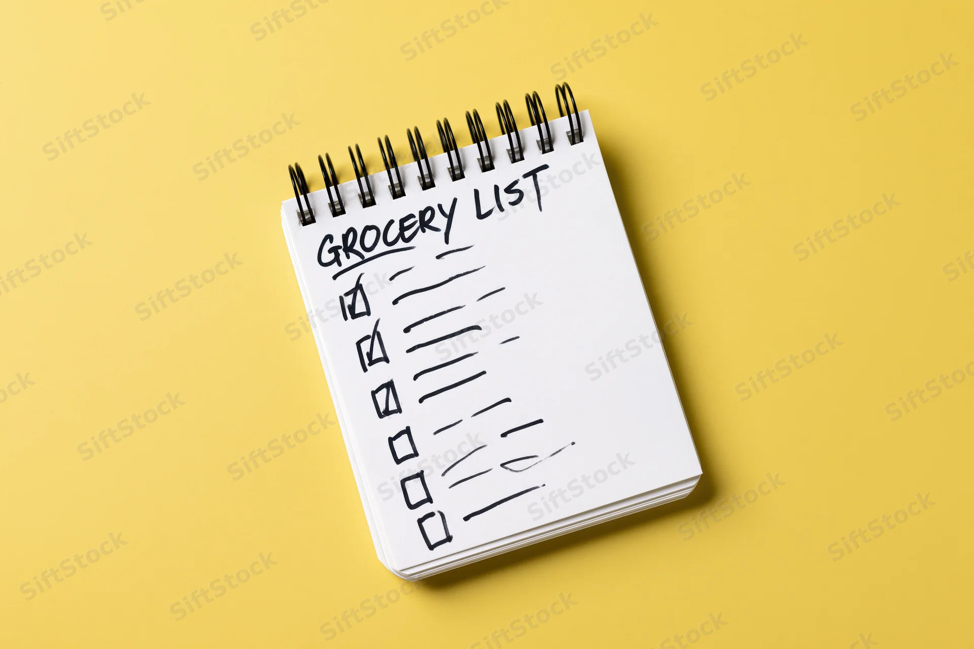 Spiral-bound notepad with handwritten grocery list and checkboxes on yellow background