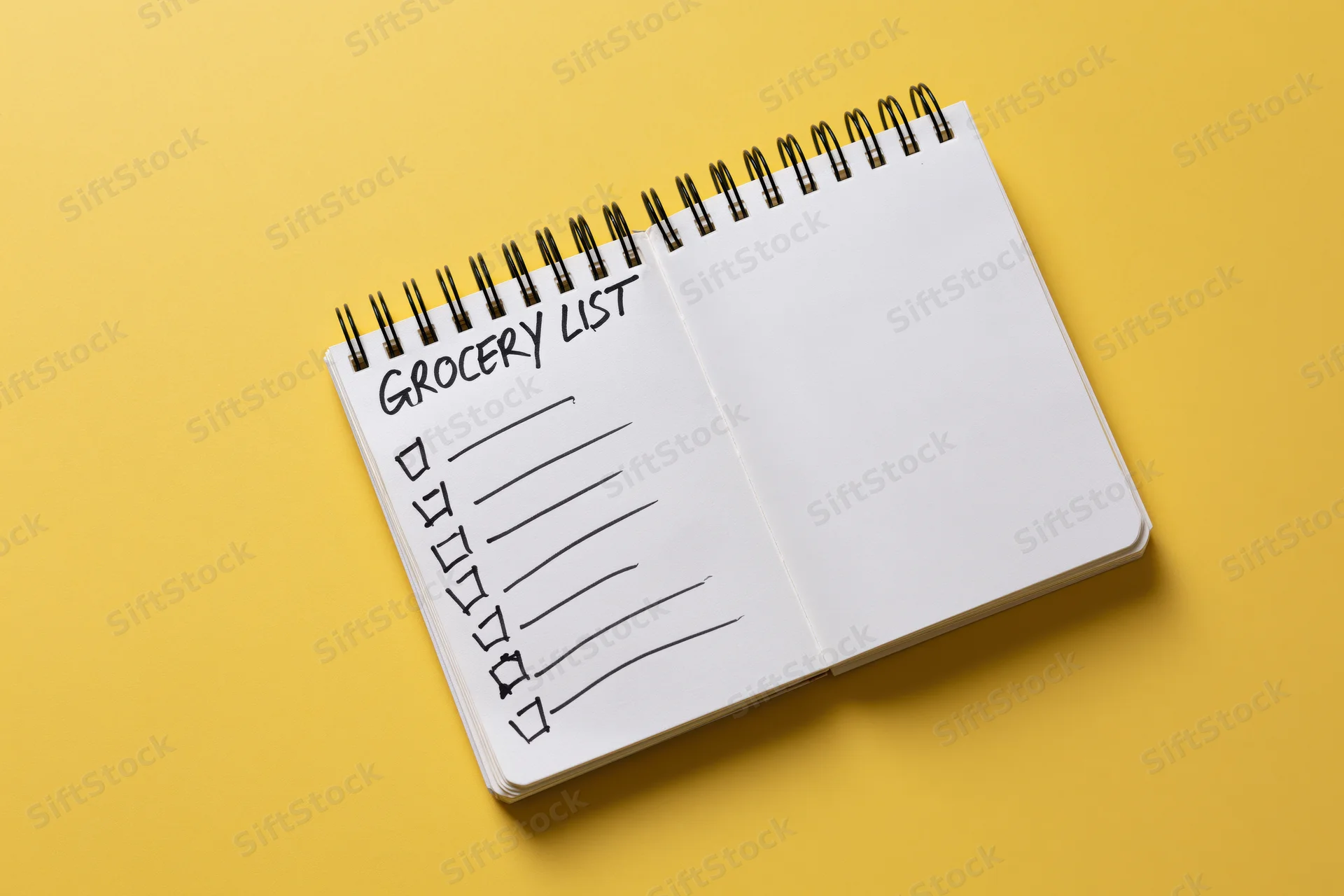 Open spiral-bound notepad with grocery list and checkboxes on yellow surface