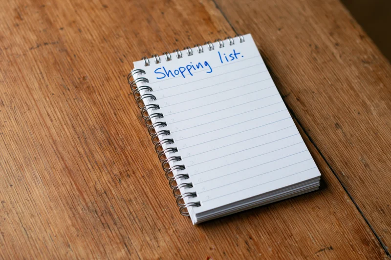 Spiral-bound notepad with handwritten shopping list on lined paper resting on wooden table