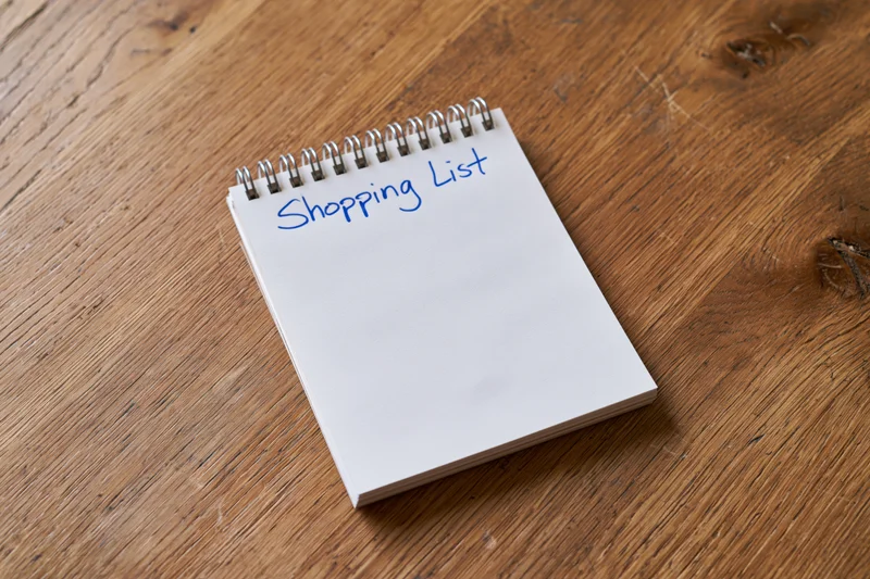 Spiral-bound notepad with shopping list written in blue ink on wooden table