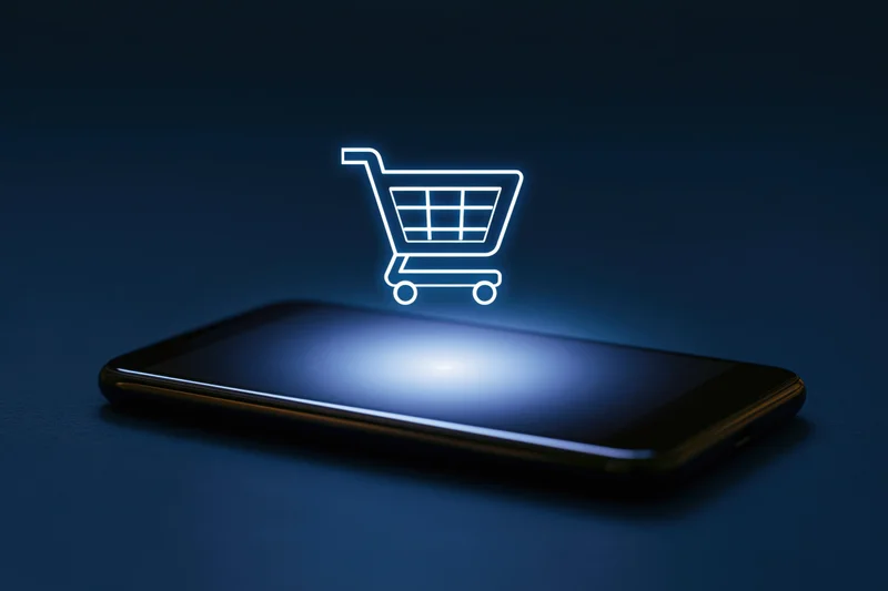 Smartphone with glowing shopping cart icon hovering above its screen on dark surface