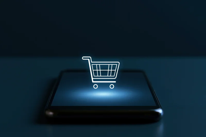 Smartphone with glowing shopping cart icon on dark surface