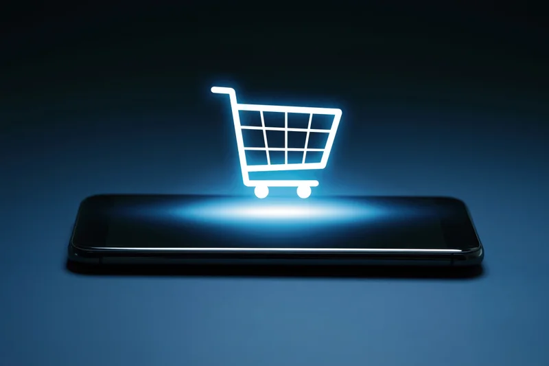 Glowing shopping cart icon hovering above a smartphone on a dark surface