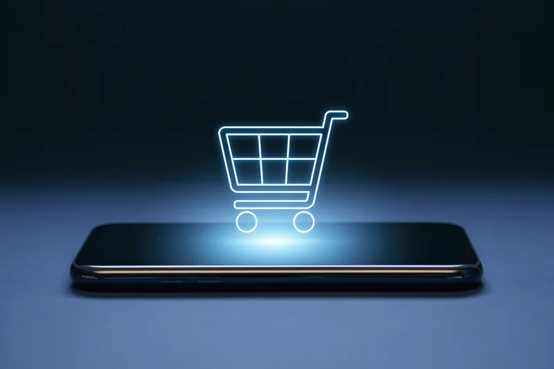 Smartphone lying flat with glowing shopping cart hovering above its screen on dark surface