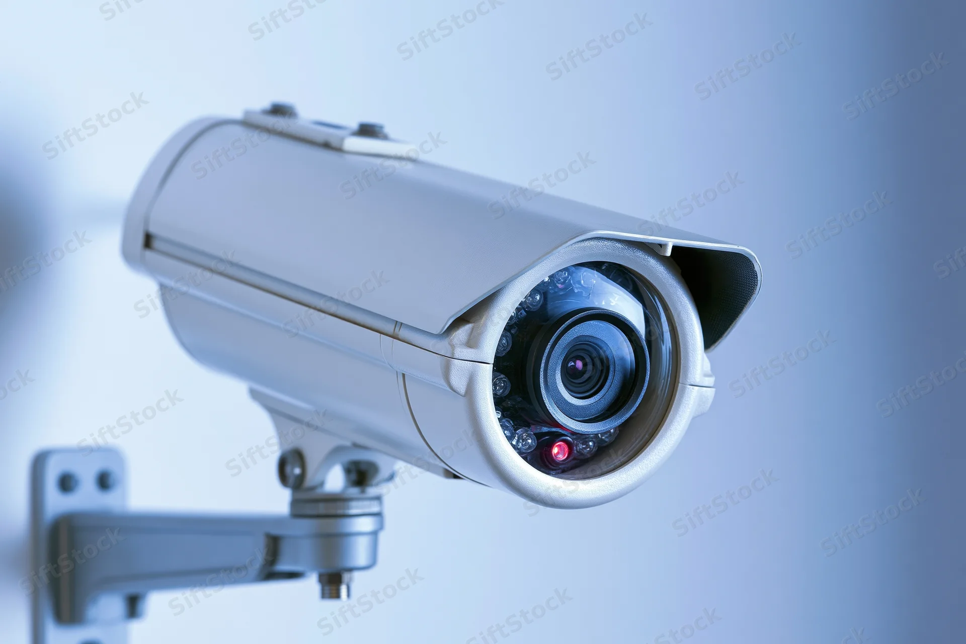 White cctv security camera mounted on metal bracket against light wall