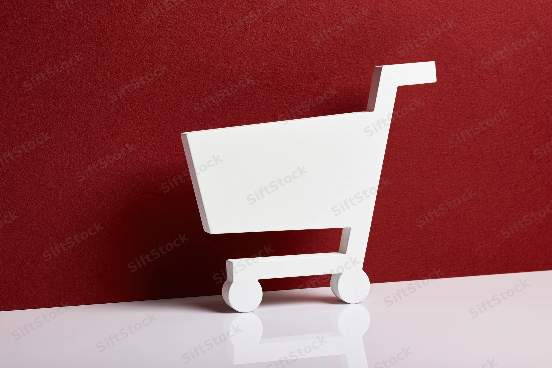 White shopping cart icon prop standing upright on a glossy white surface against a red textured background