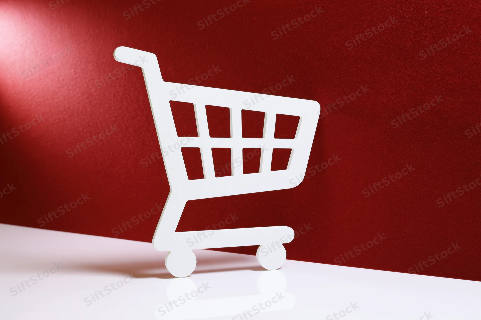 White shopping cart icon prop standing upright on a red background with copyspace