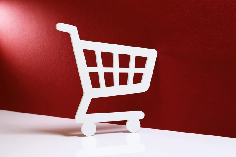 White shopping cart icon prop standing upright on a red background with copyspace