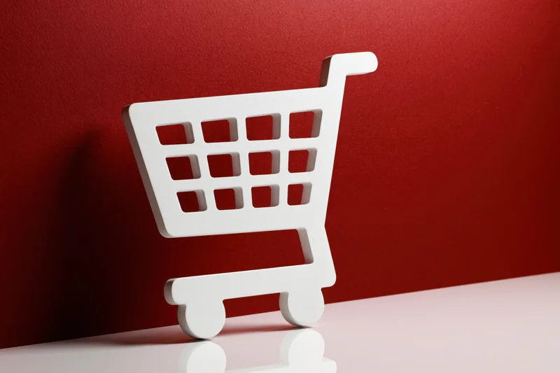 White shopping cart icon prop standing upright on a red background with reflection
