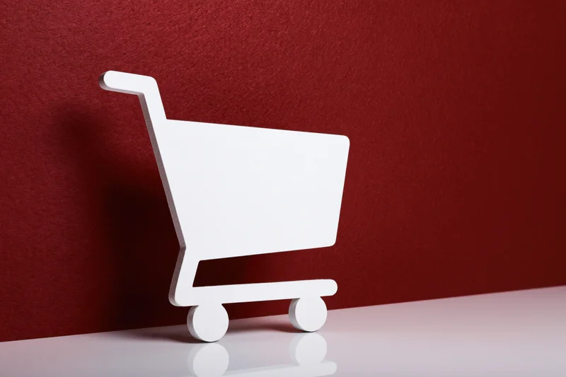 White flat shopping cart icon prop standing upright on a red textured wall with reflective white surface
