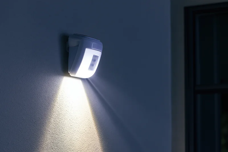 White plastic solar-powered led motion sensor light mounted on dark wall at night emitting bright beam