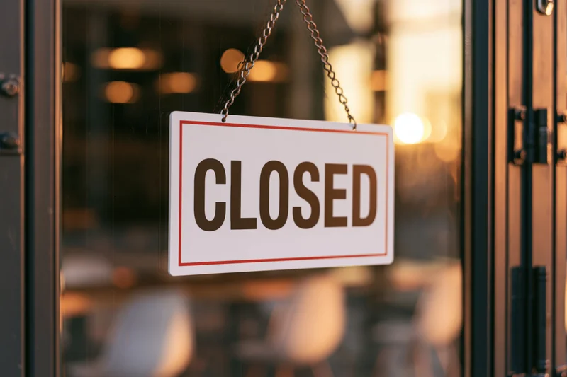 Closed sign hanging on glass door of restaurant storefront with blurred interior lighting
