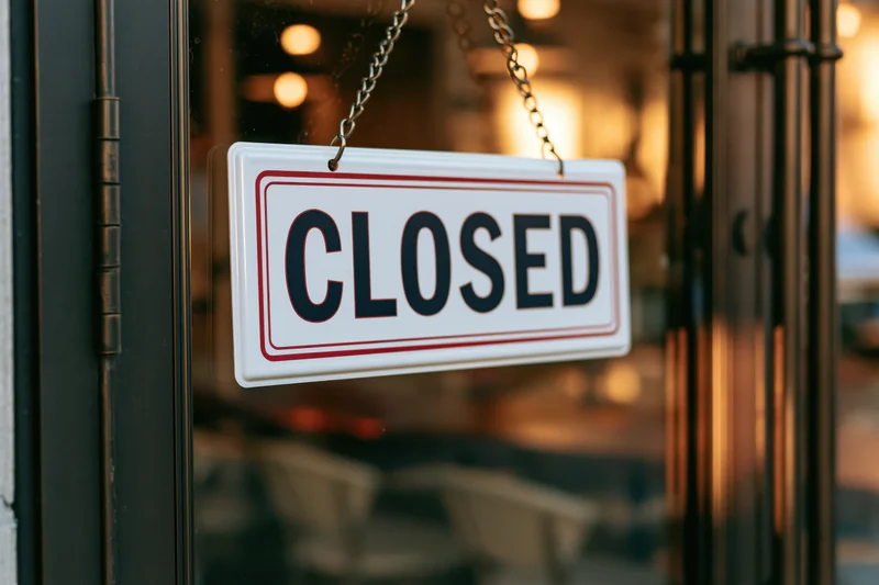 Closed sign hanging on glass door of storefront with warm interior lighting visible behind