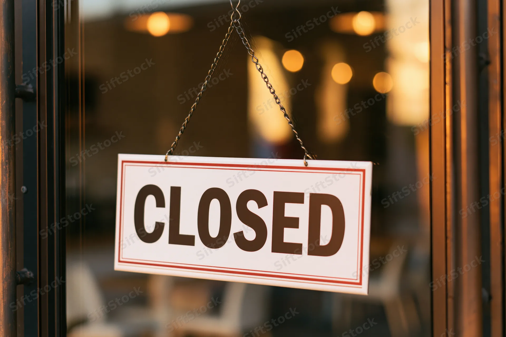 Closed sign hanging on glass door of storefront with warm interior lights visible through window