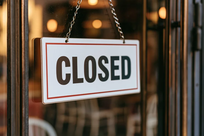 Closed sign hanging on glass storefront door of a restaurant with warm interior lights visible behind