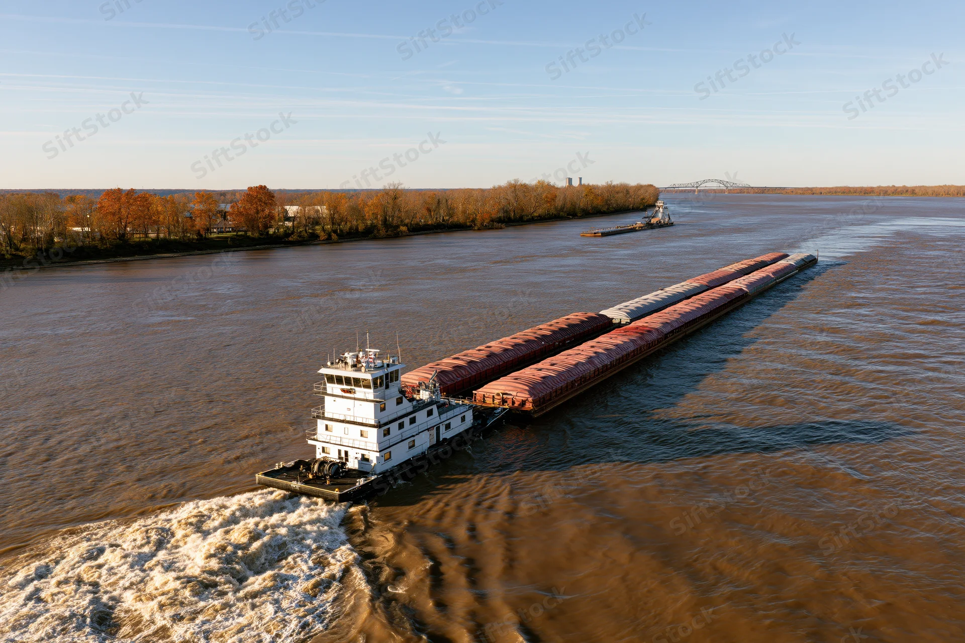 White towboat pushing a long string of covered cargo barges on a wide river