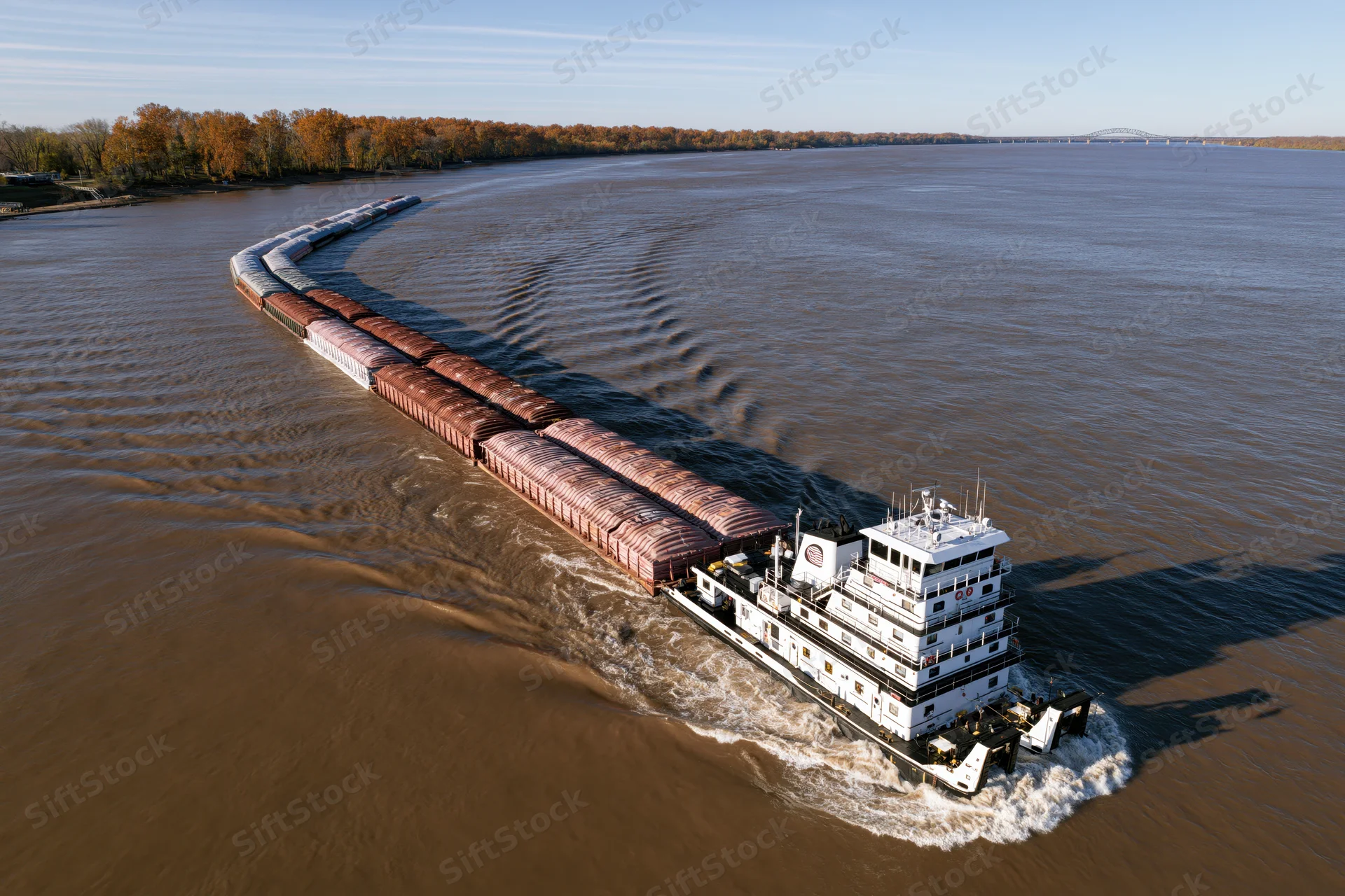 White towboat pushing a long string of covered cargo barges on a wide river