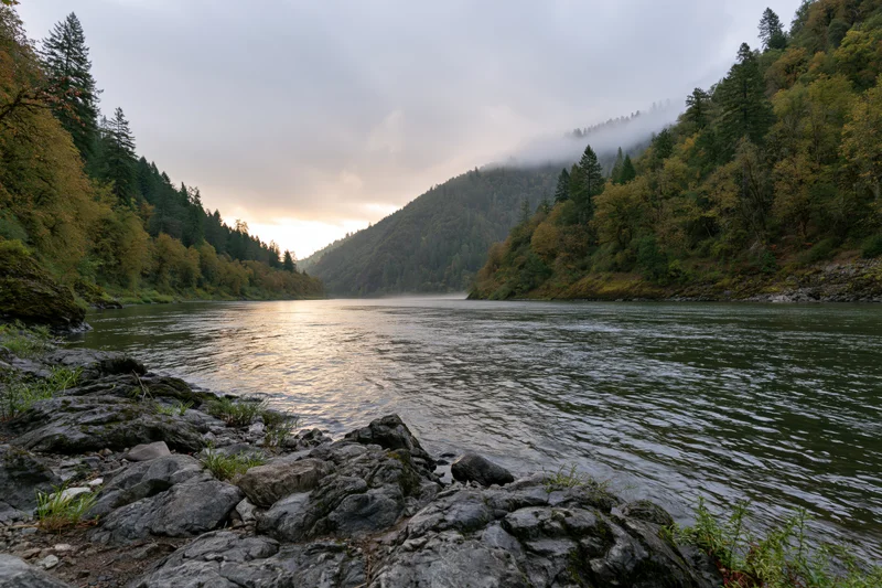 Wide river flowing through forested canyon with misty mountains and autumn foliage