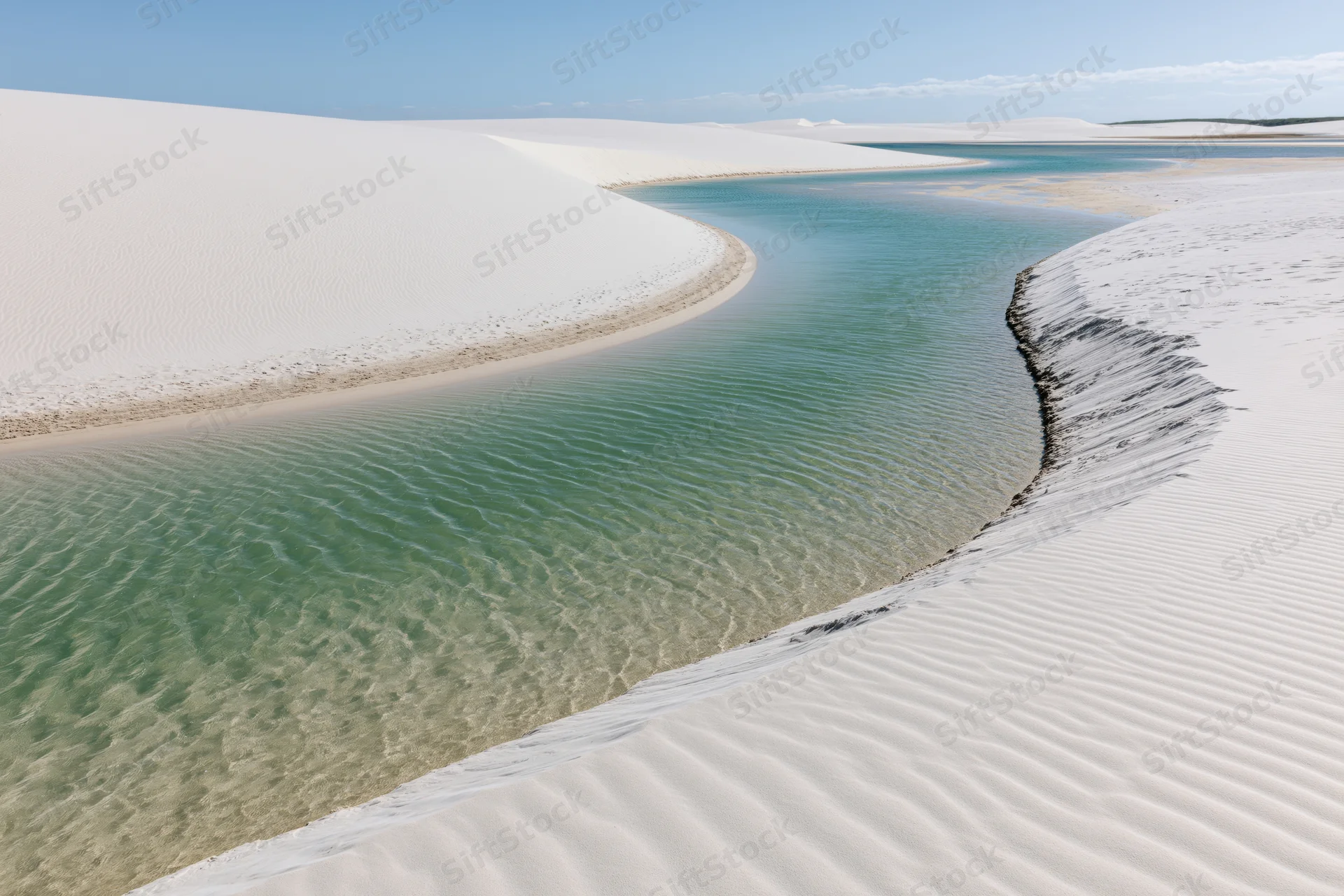 Winding turquoise lagoon between white sand dunes in a desert landscape