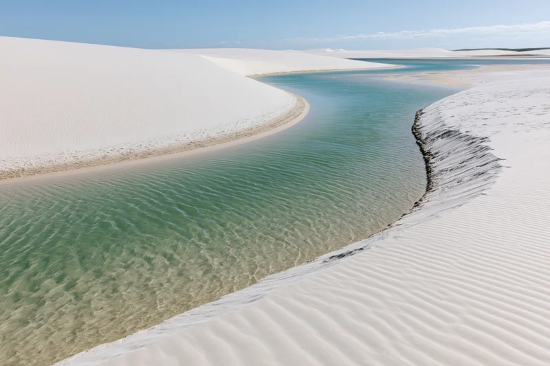 Winding turquoise lagoon between white sand dunes in a desert landscape
