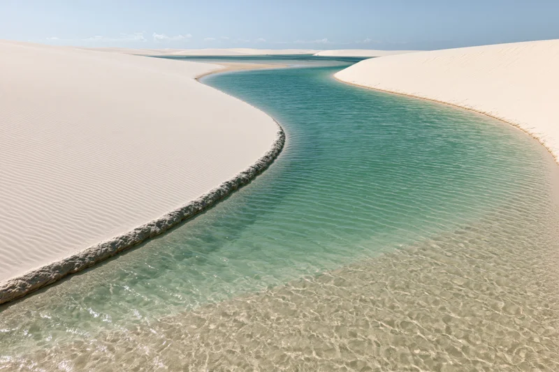 Winding turquoise lagoon between white sand dunes in a desert landscape