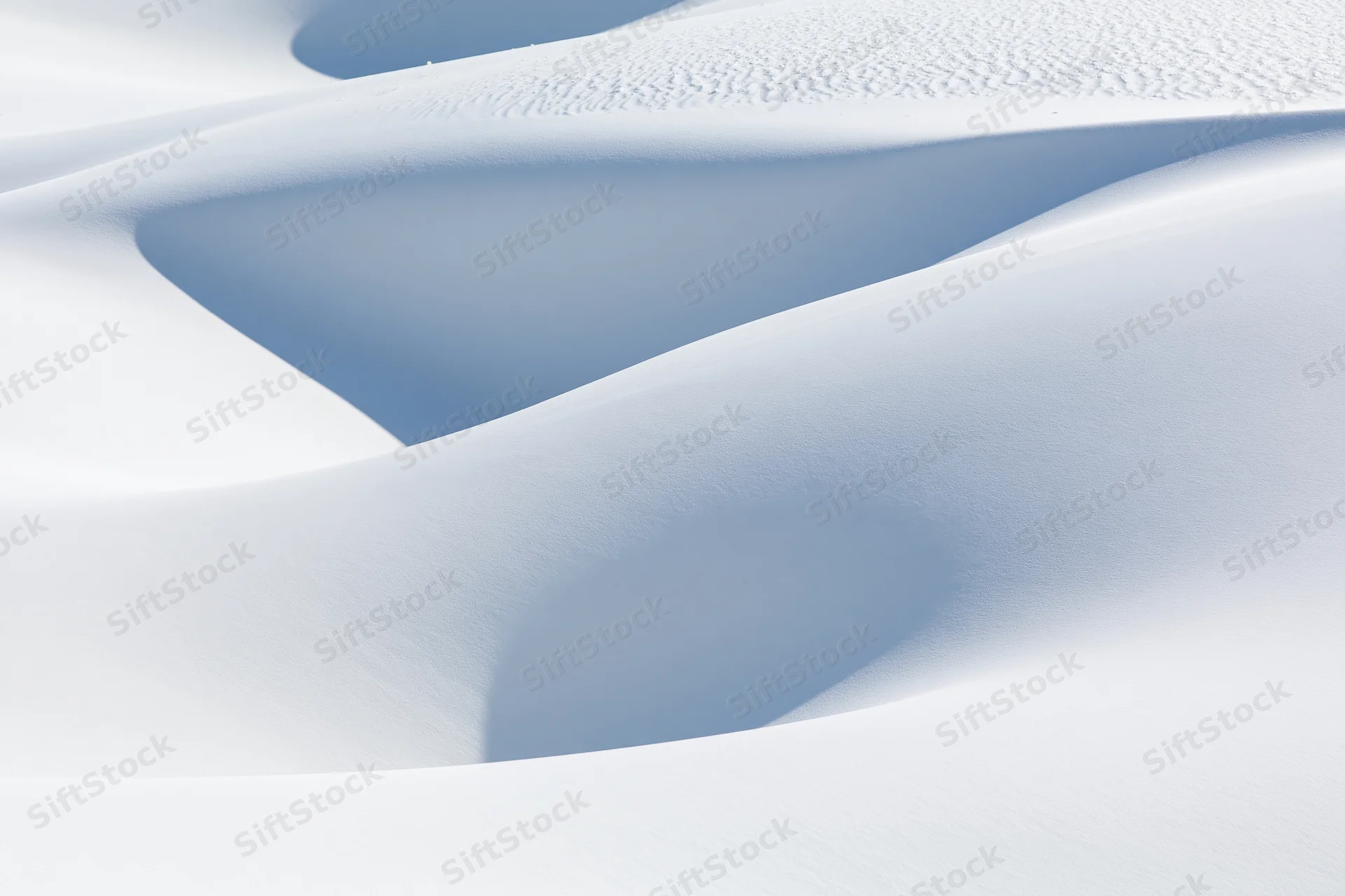 Smooth white gypsum sand dunes forming undulating curves under bright light in a desert landscape