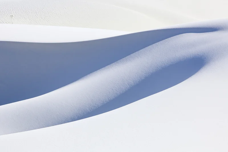 Smooth white gypsum sand dunes forming flowing curves under bright light in a desert landscape