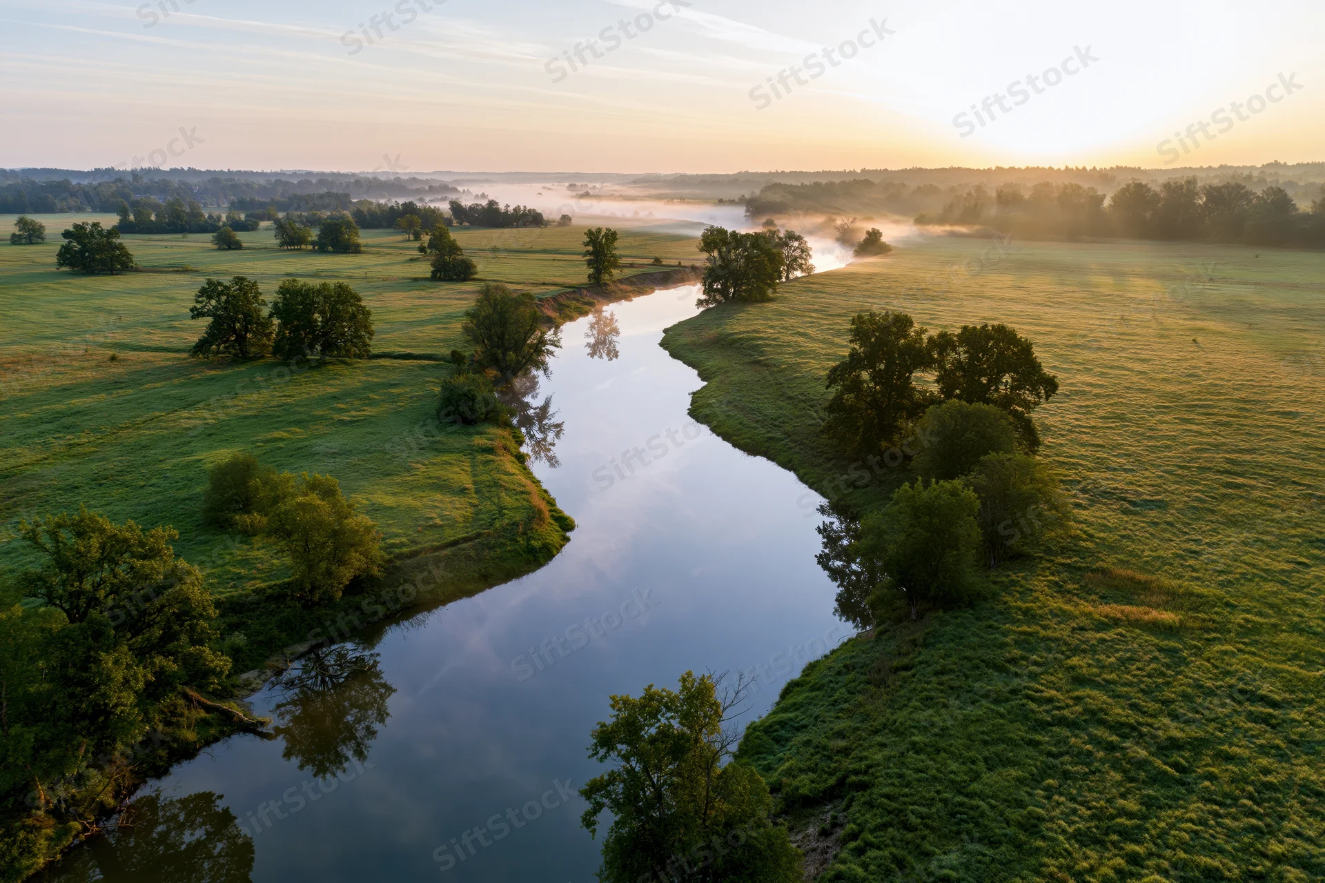 Aerial drone view of a winding river snaking through green meadows at sunrise