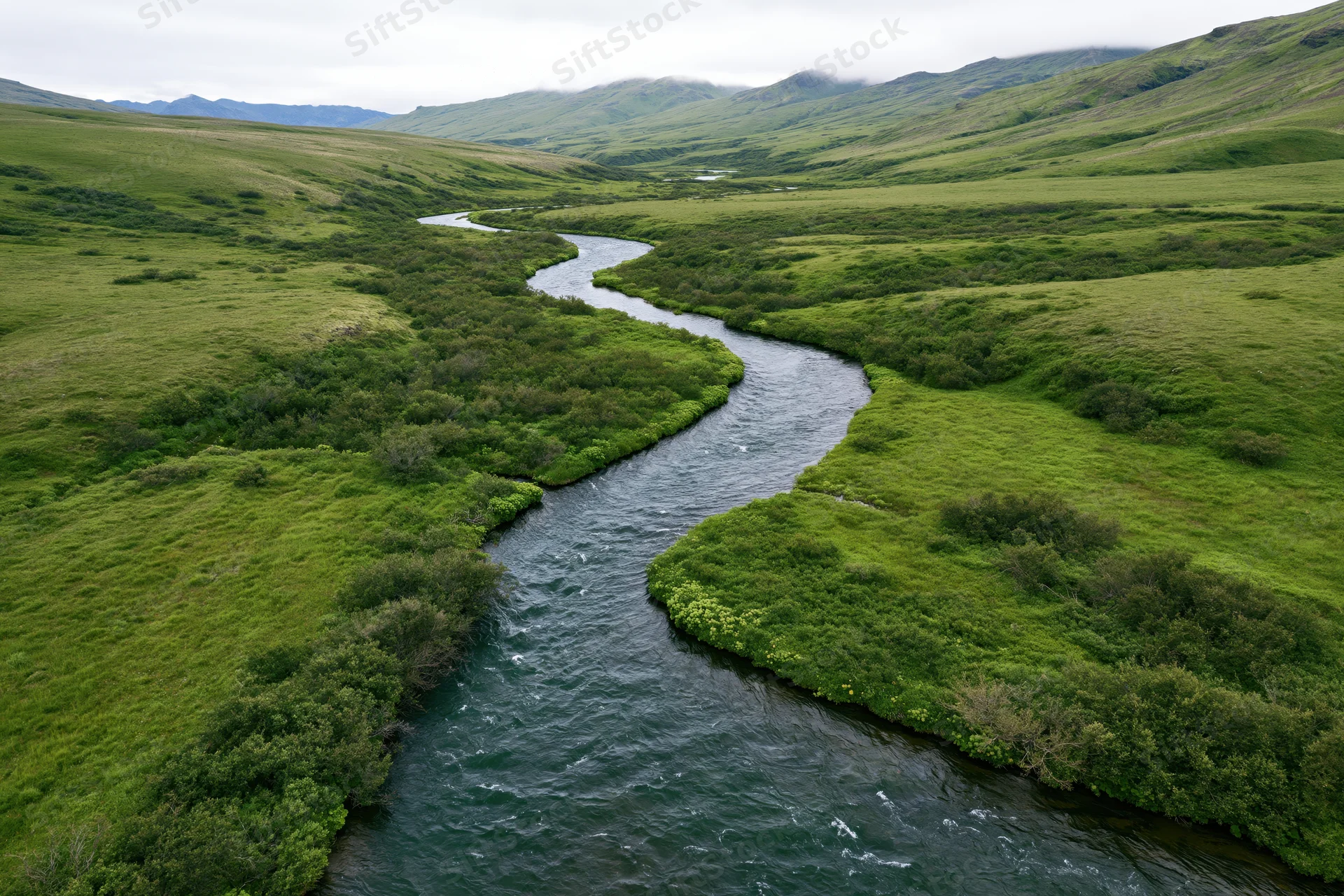 Aerial drone view of a winding river flowing through lush green valley with hills and meadows