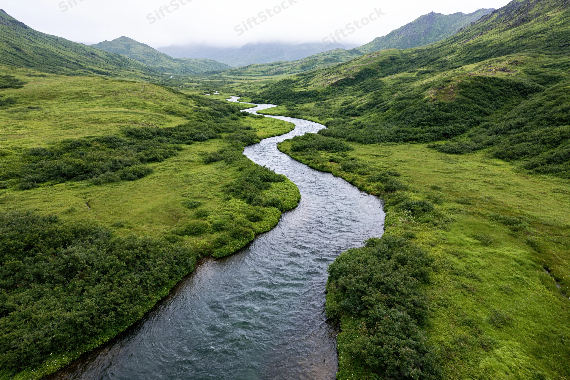 Aerial drone view of a winding river flowing through a lush green valley surrounded by mountains