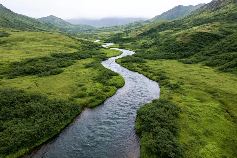 Aerial drone view of a winding river flowing through a lush green valley surrounded by mountains