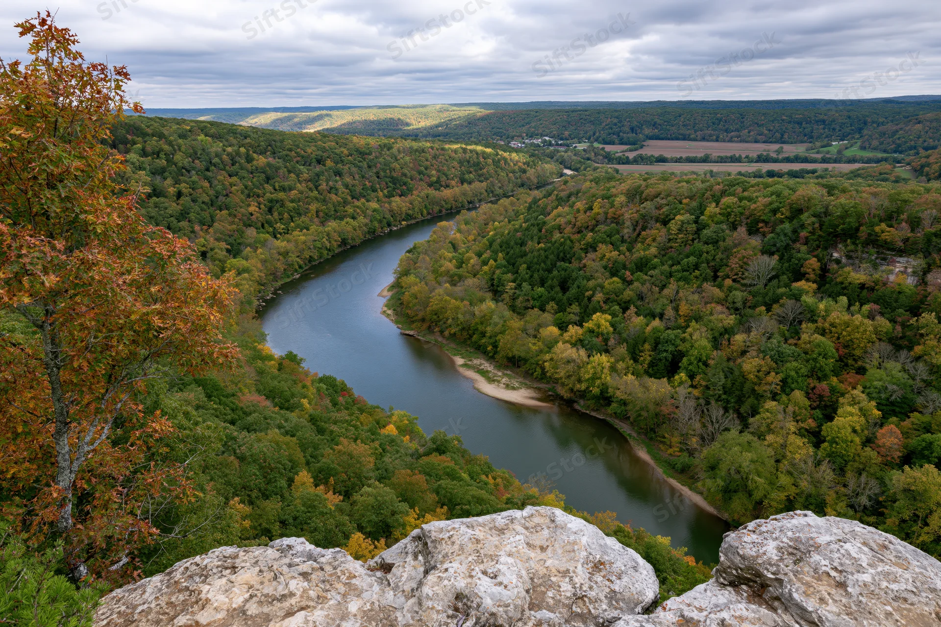 Aerial view of a winding river cutting through a forested valley in autumn