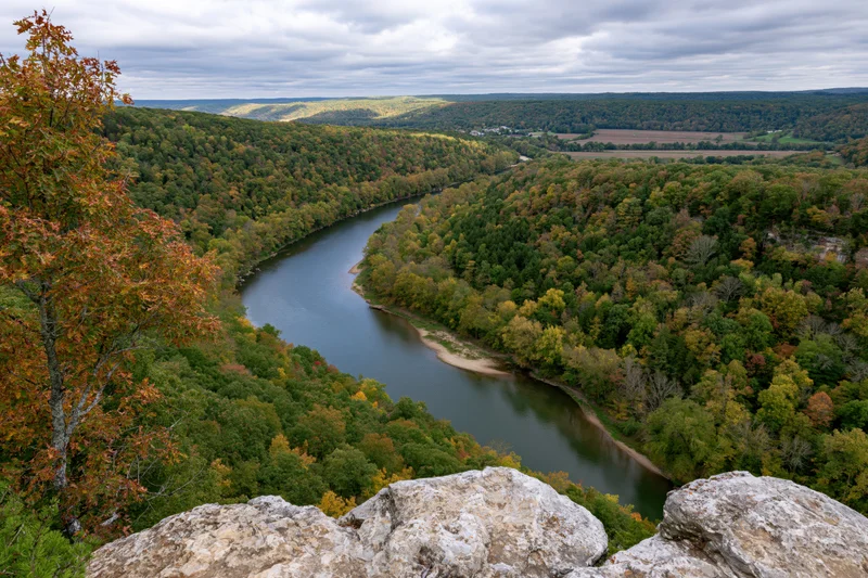 Aerial view of a winding river cutting through a forested valley in autumn