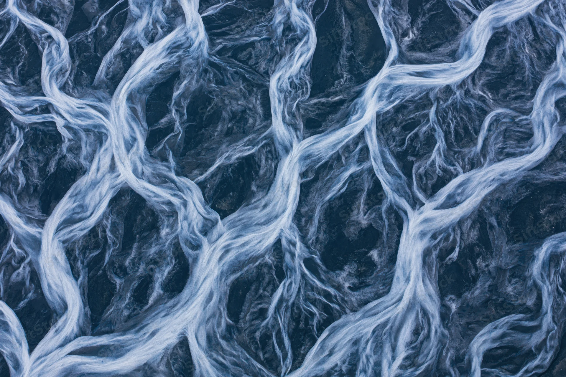 Aerial topdown view of a braided glacial river delta flowing through rocky terrain